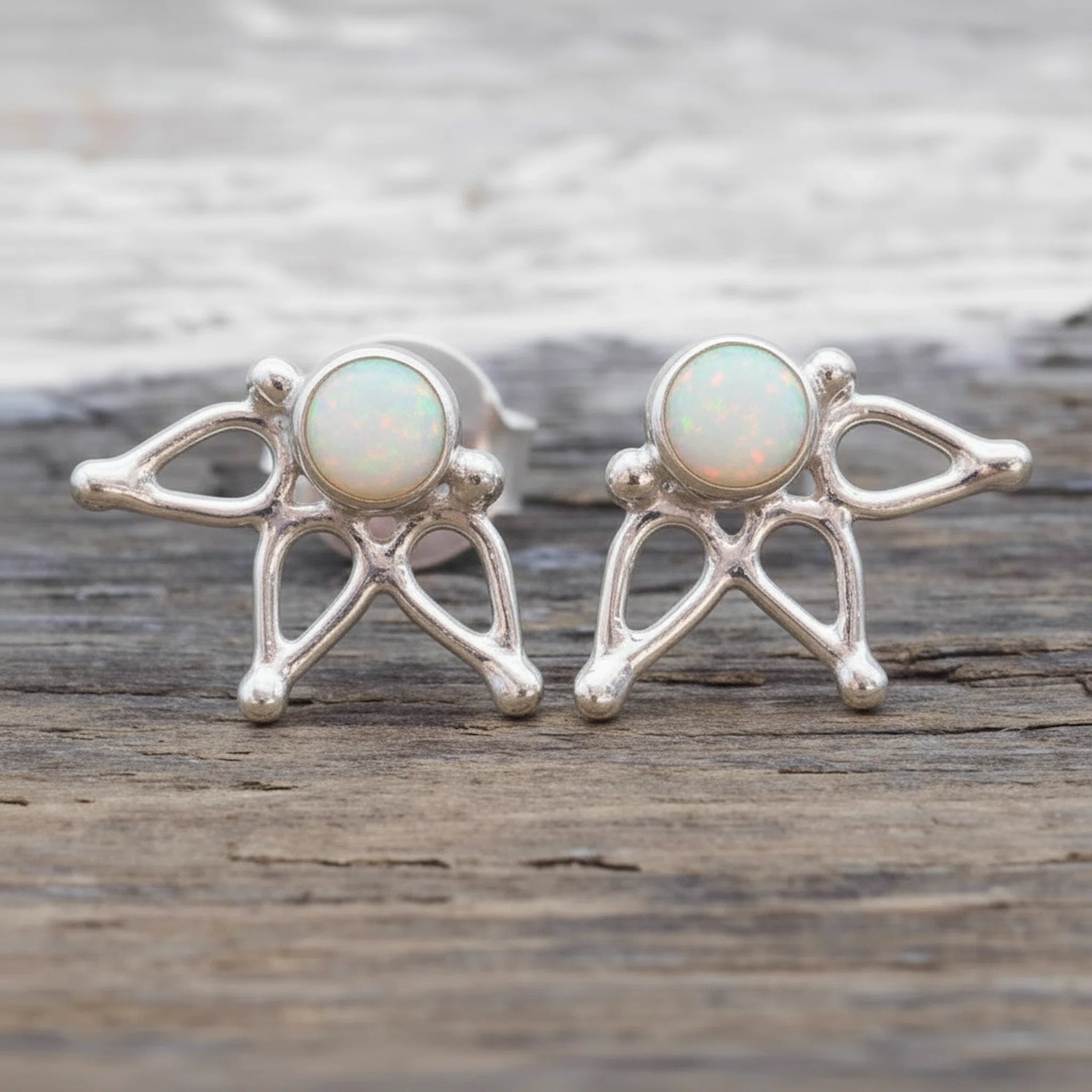 A pair of sterling silver stud earrings featuring round natural australian white opals, displayed on a rustic wooden surface.