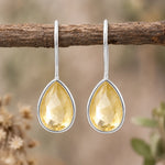 Pair of sterling silver natural citrine teardrop hook earrings hanging from a branch