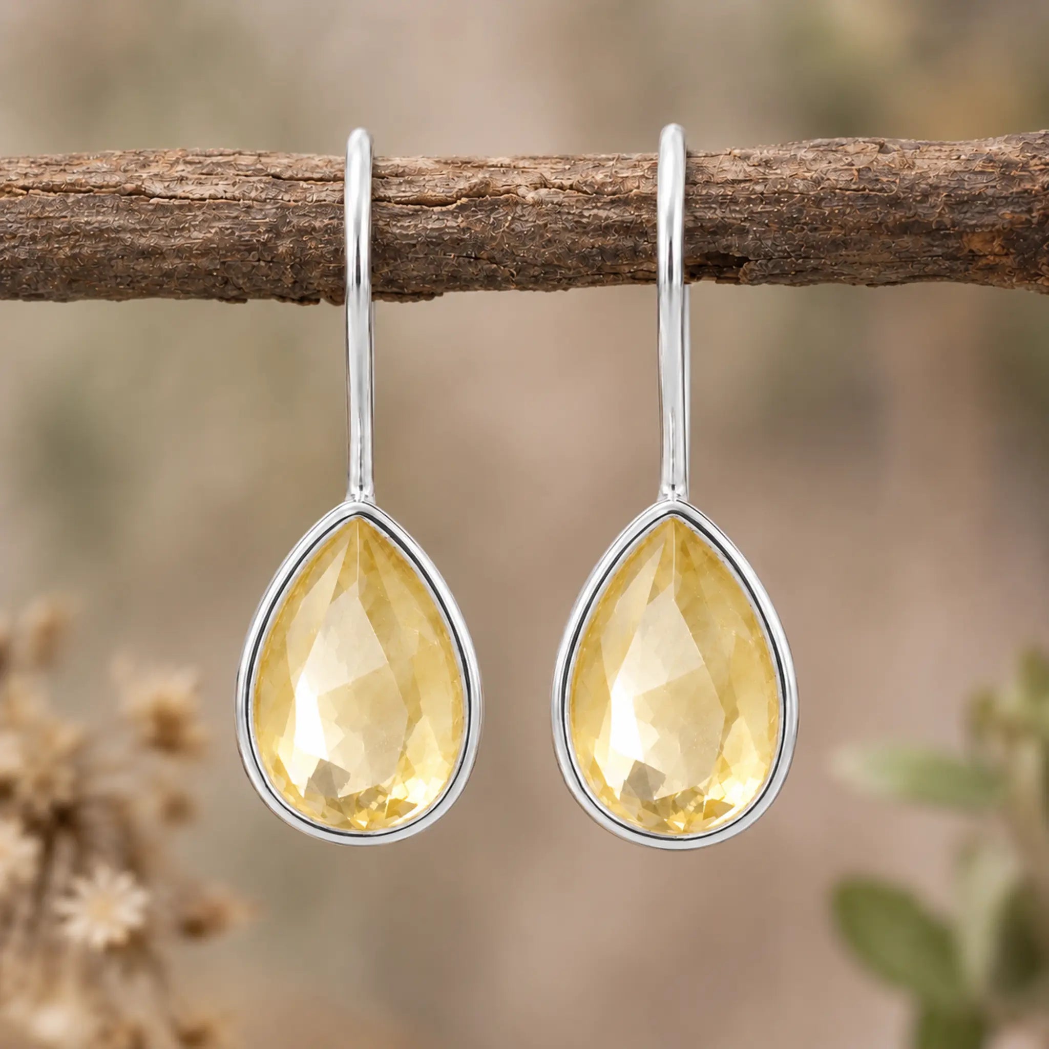 Pair of sterling silver natural citrine teardrop hook earrings hanging from a branch