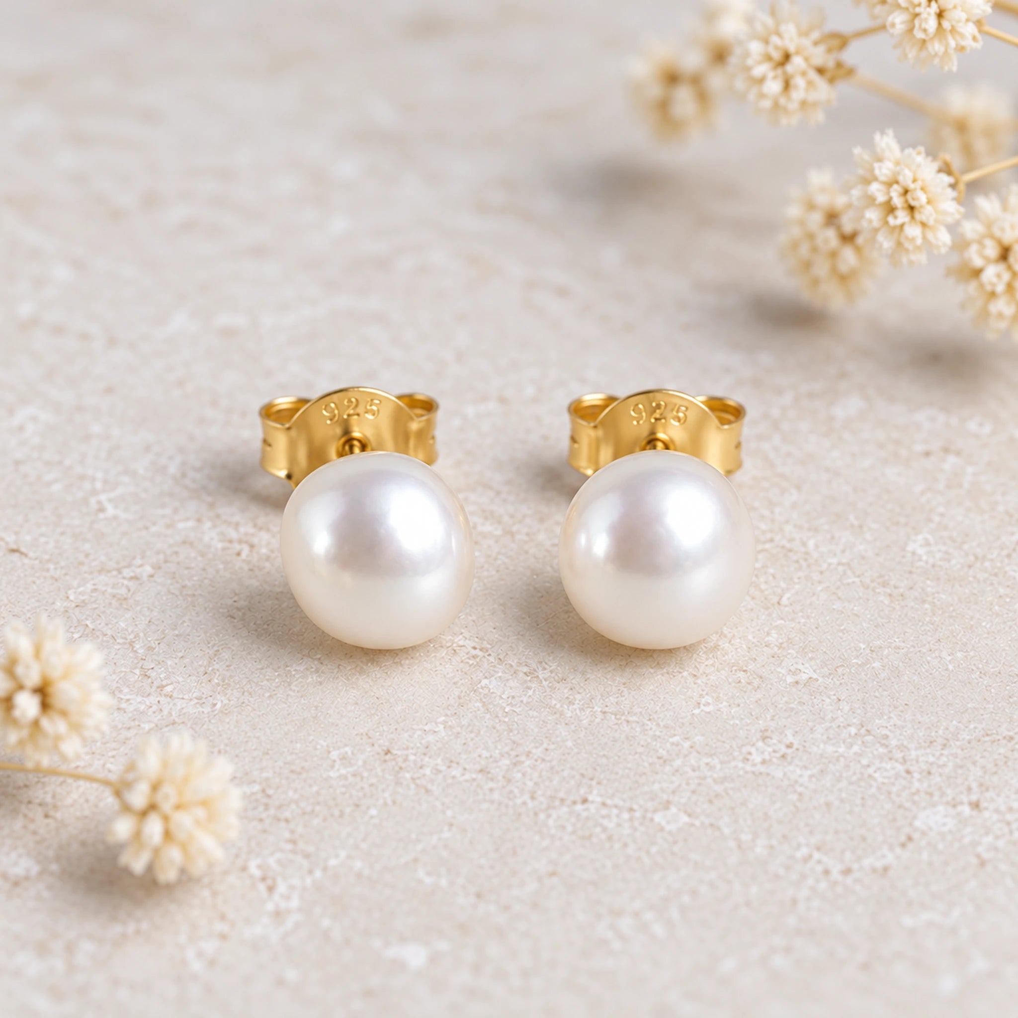 Gold plated freshwater pearl earrings, a pair of 7 mm pearl studs on a stone background with dried flowers