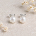 Sterling silver freshwater pearl earrings, a pair of white pearl studs on a stone background with dried flowers