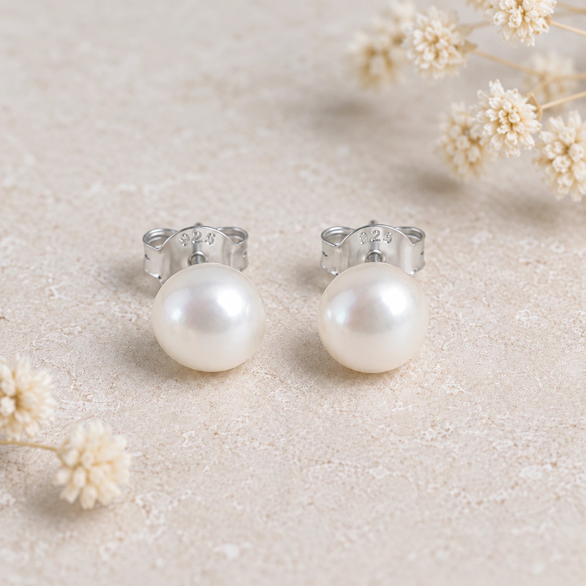 Sterling silver freshwater pearl earrings, a pair of white pearl studs on a stone background with dried flowers