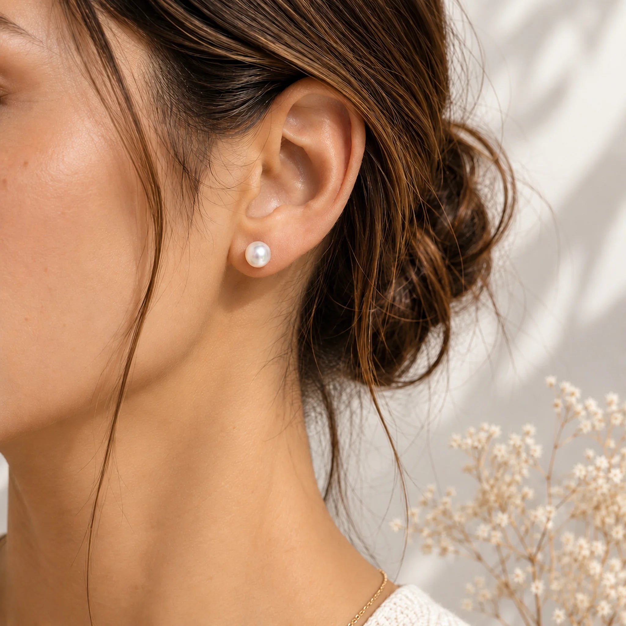 Freshwater pearl earrings worn, a single white pearl stud on the earlobe with hair in a low bun