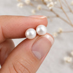 Freshwater pearl earrings held between fingertips to show the 7 mm round pearl size