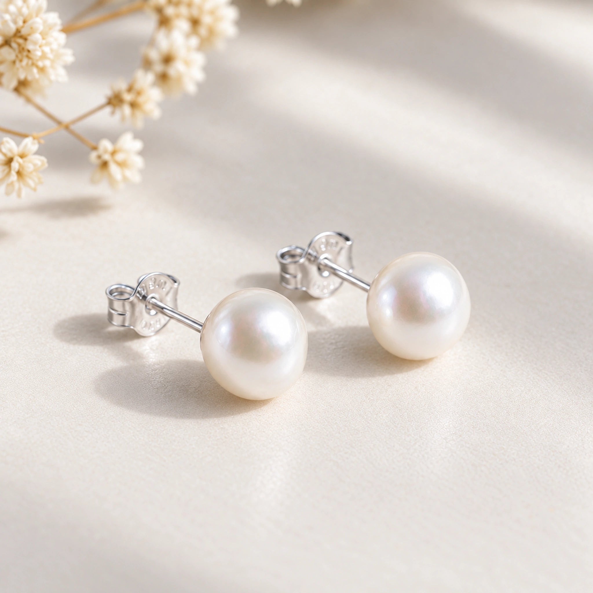 Pair of sterling silver freshwater pearl earrings with butterfly backs on a cream background