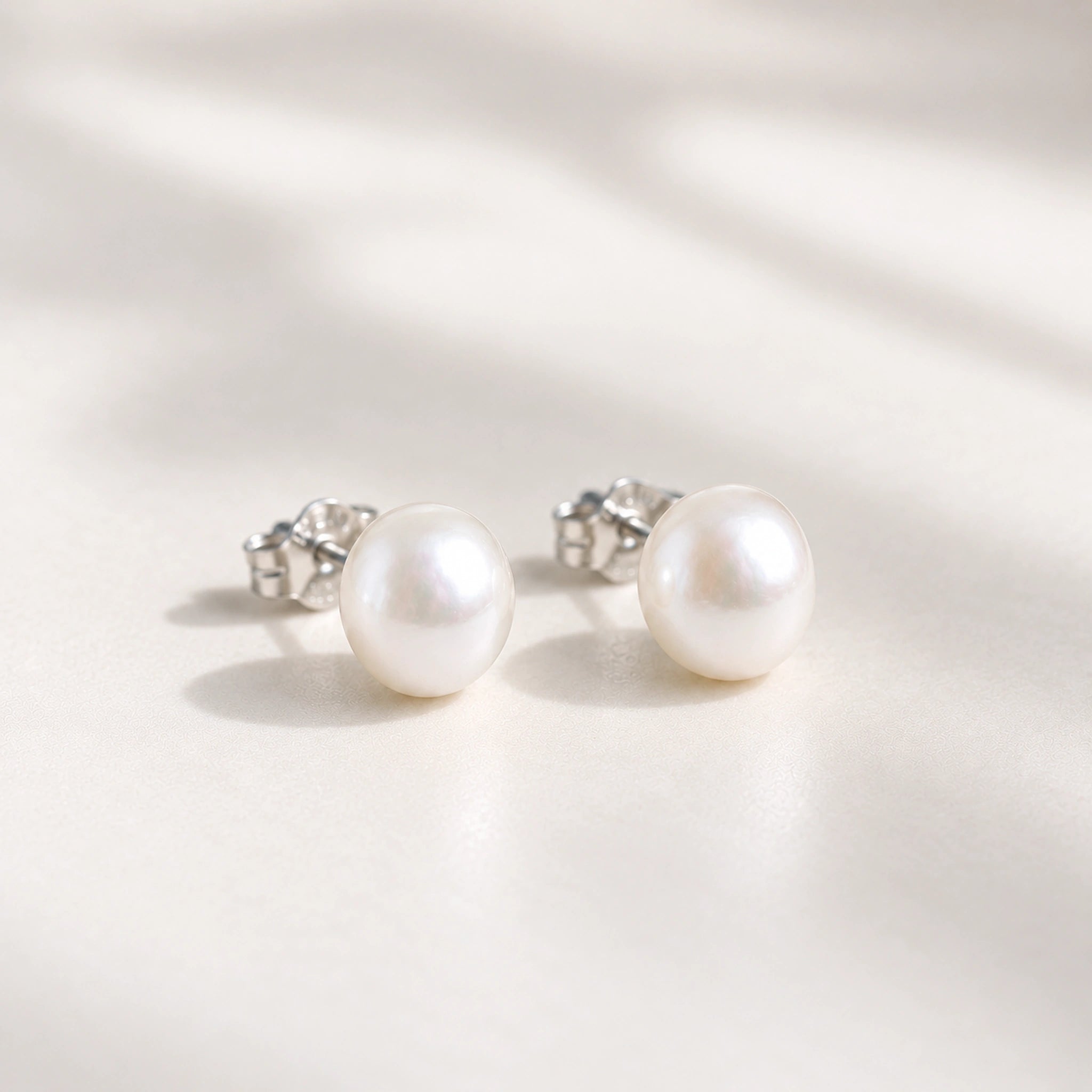 Sterling silver freshwater pearl earrings, a pair of white pearl studs in soft light on cream