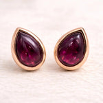 Pair of rose gold january birthstone earrings with teardrop-shaped natural garnet gemstones on a light background