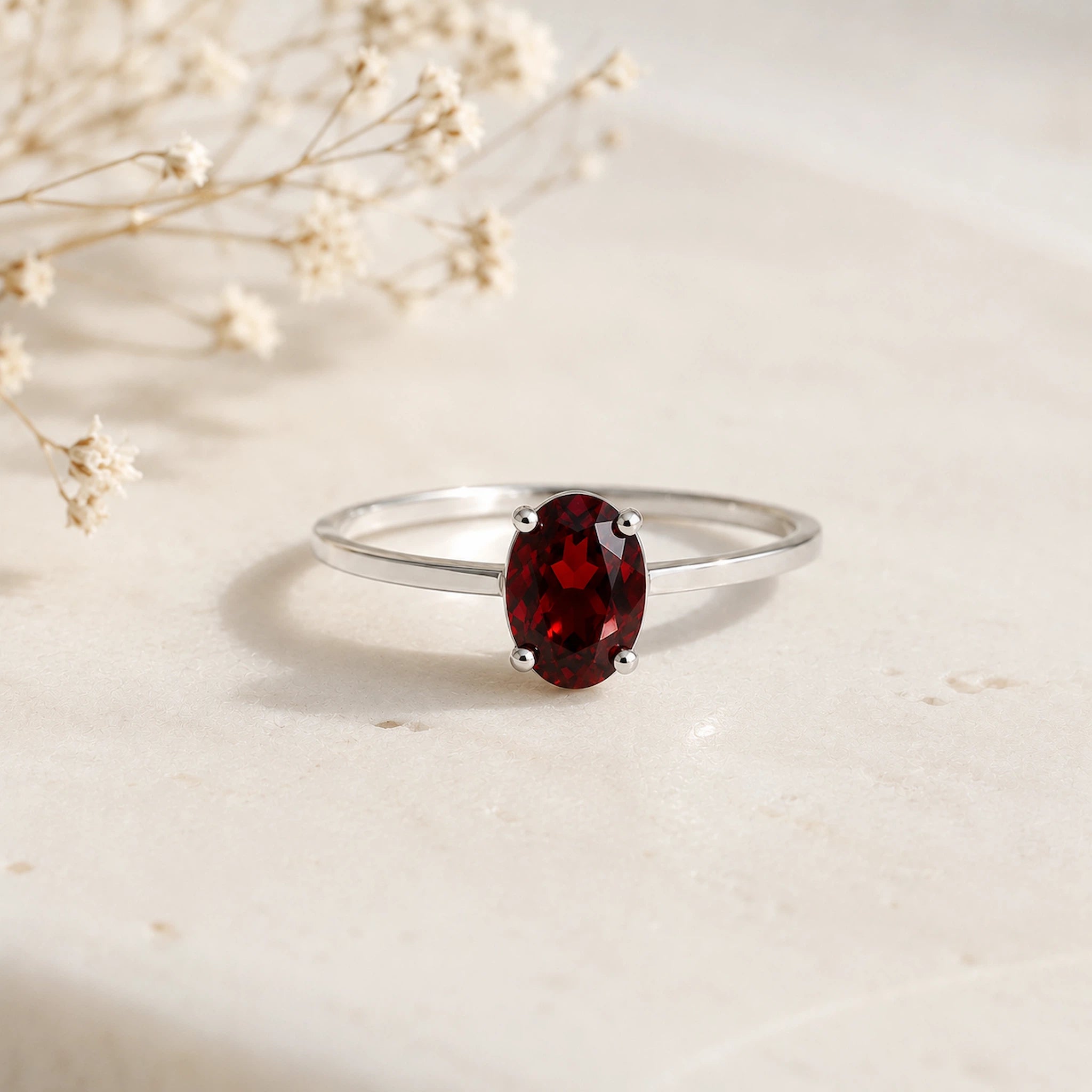 Sterling Silver Claw Set ring with oval faceted natural garnet gemstone on a white surface.