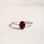 Sterling Silver Claw Set ring with oval faceted natural garnet gemstone on a white surface.