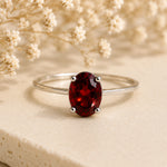 Sterling Silver Claw Set ring with oval faceted natural garnet gemstone on a light surface.