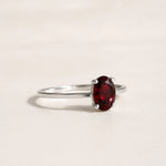 side view of a Sterling Silver Claw Set ring with oval faceted natural garnet gemstone on a white surface.