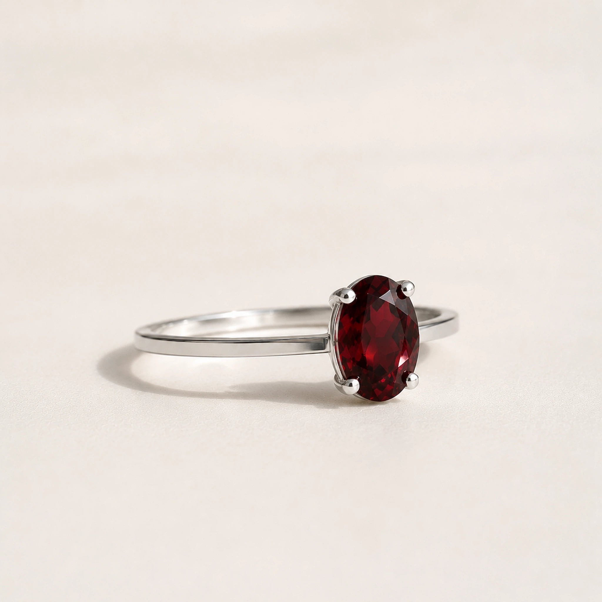 side view of a Sterling Silver Claw Set ring with oval faceted natural garnet gemstone on a white surface.