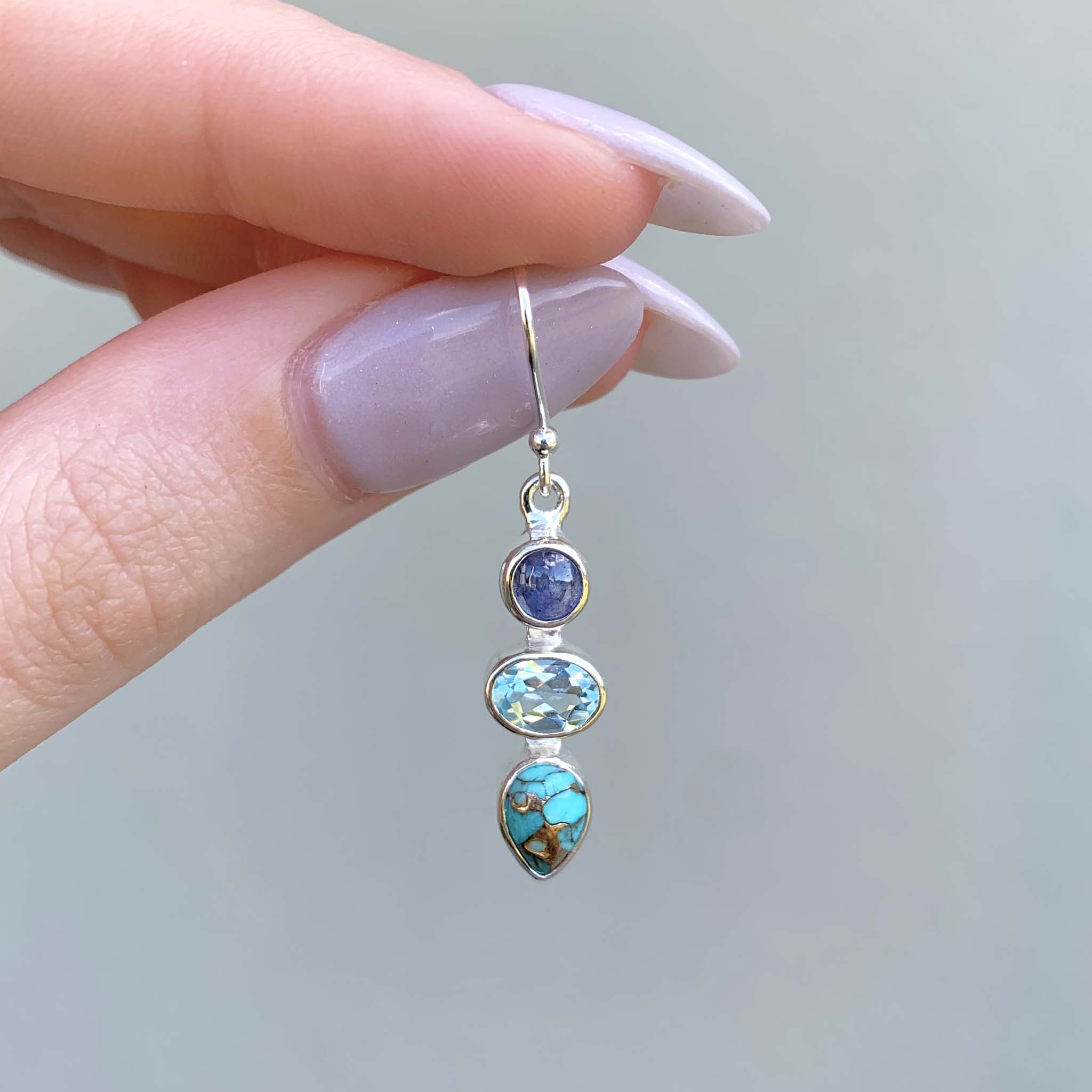 natural gemstone earrings made with tanzanite, topaz and turquoise being held