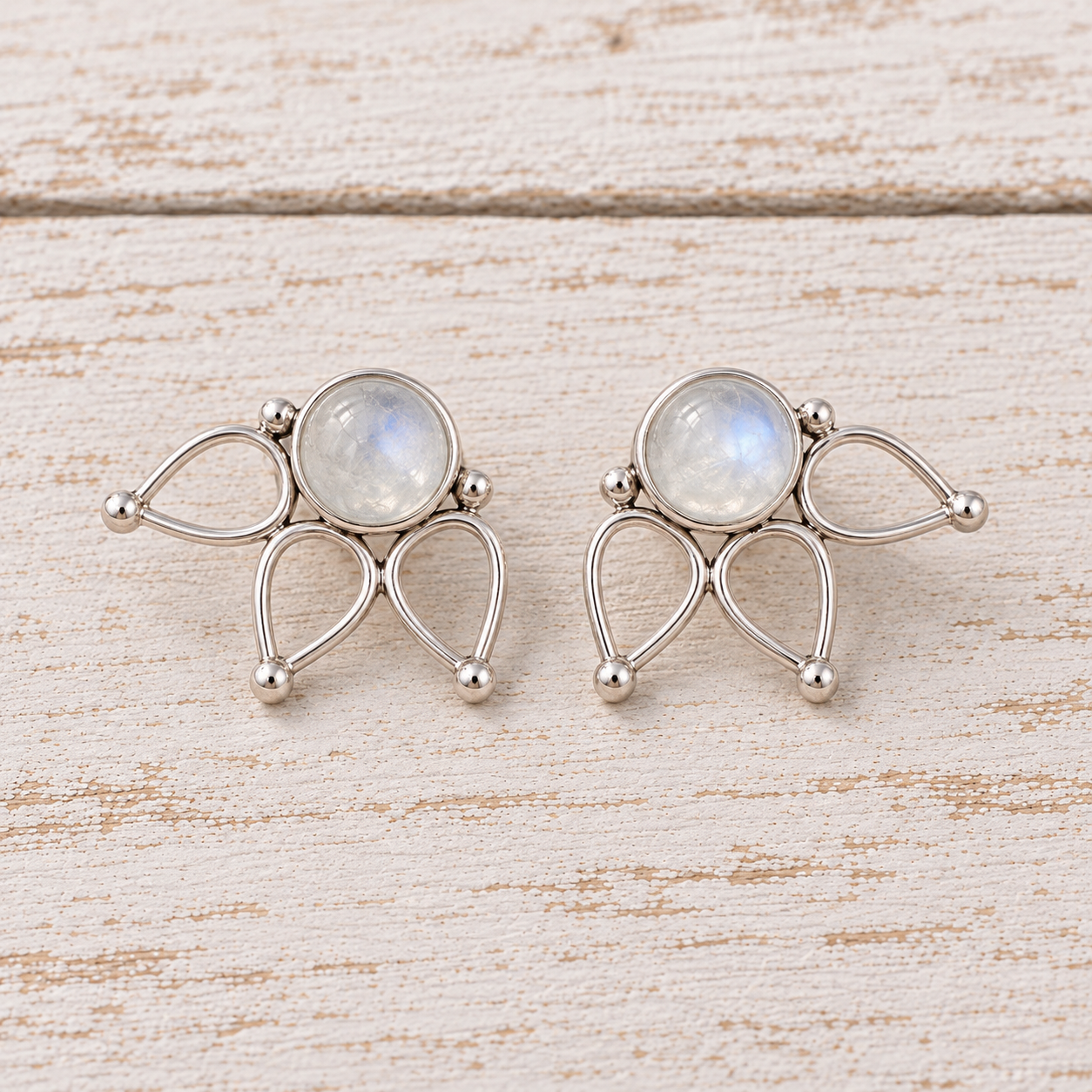 A pair of sterling silver moonstone lotus stud earrings with oval milky natural moonstones, displayed on a light, rustic wooden surface.
