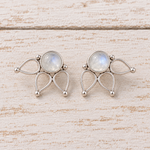 A pair of sterling silver moonstone lotus stud earrings with oval milky natural moonstones, displayed on a light, rustic wooden surface.