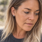 A close-up of a woman with blonde hair wearing a small silver natural moonstone stud earring with a light blue stone.