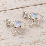 A pair of silver stud earrings with teardrop-shaped metal settings and round iridescent moonstone centers, displayed on a light wood surface.