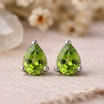 Close-up of faceted pear-shaped peridot stud earrings in sterling silver claw settings on linen
