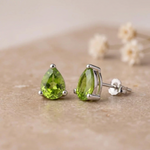 Peridot stud earrings side view showing the sterling silver claw setting and butterfly back on beige stone