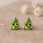 Pair of pear-shaped peridot stud earrings in sterling silver claws on beige stone with small white flowers