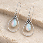 Angled pair of natural opal teardrop French hook earrings with silver bead detail, on a cream stone block