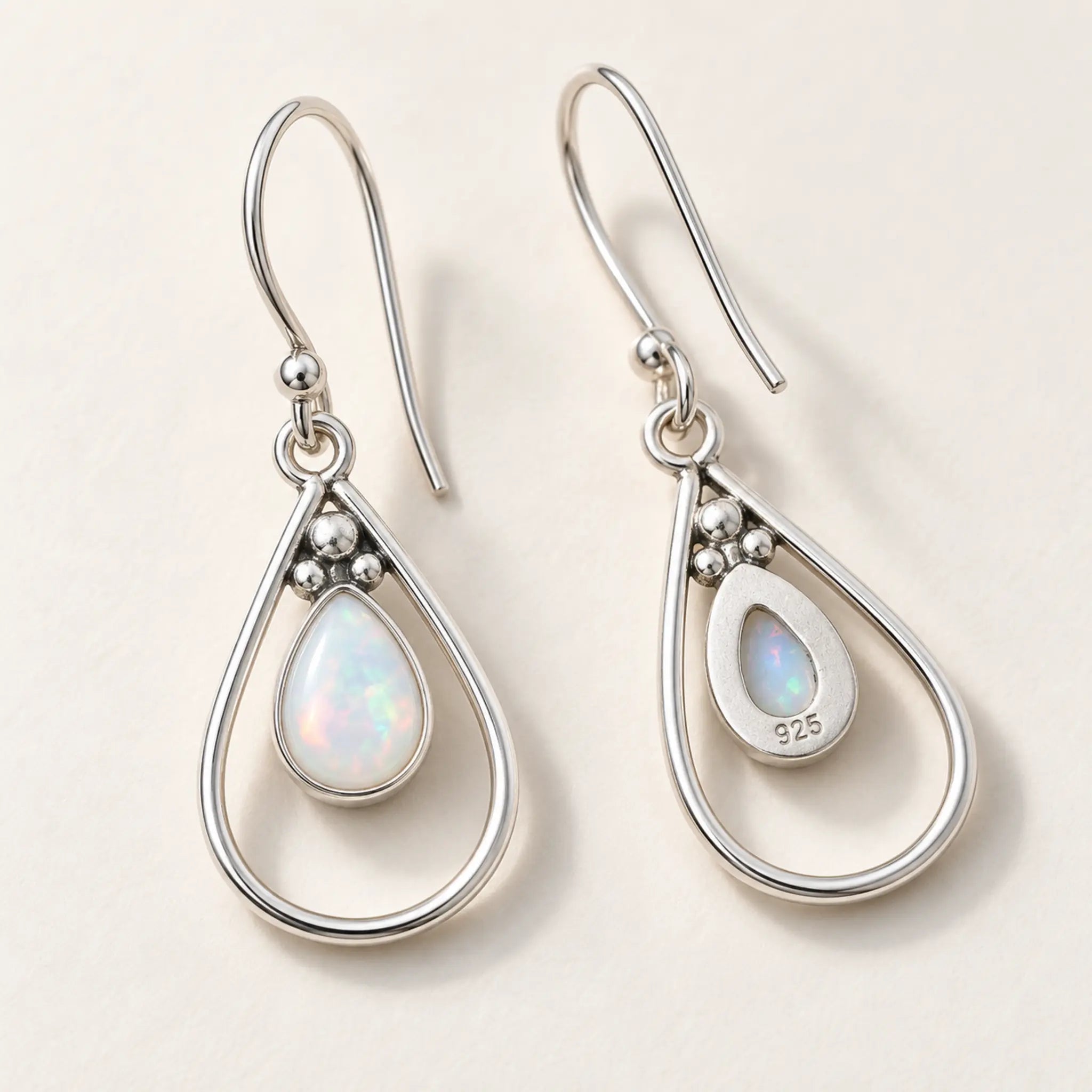 Front and back of opal teardrop French hook earrings, showing the 925 stamp on the back, on a cream background