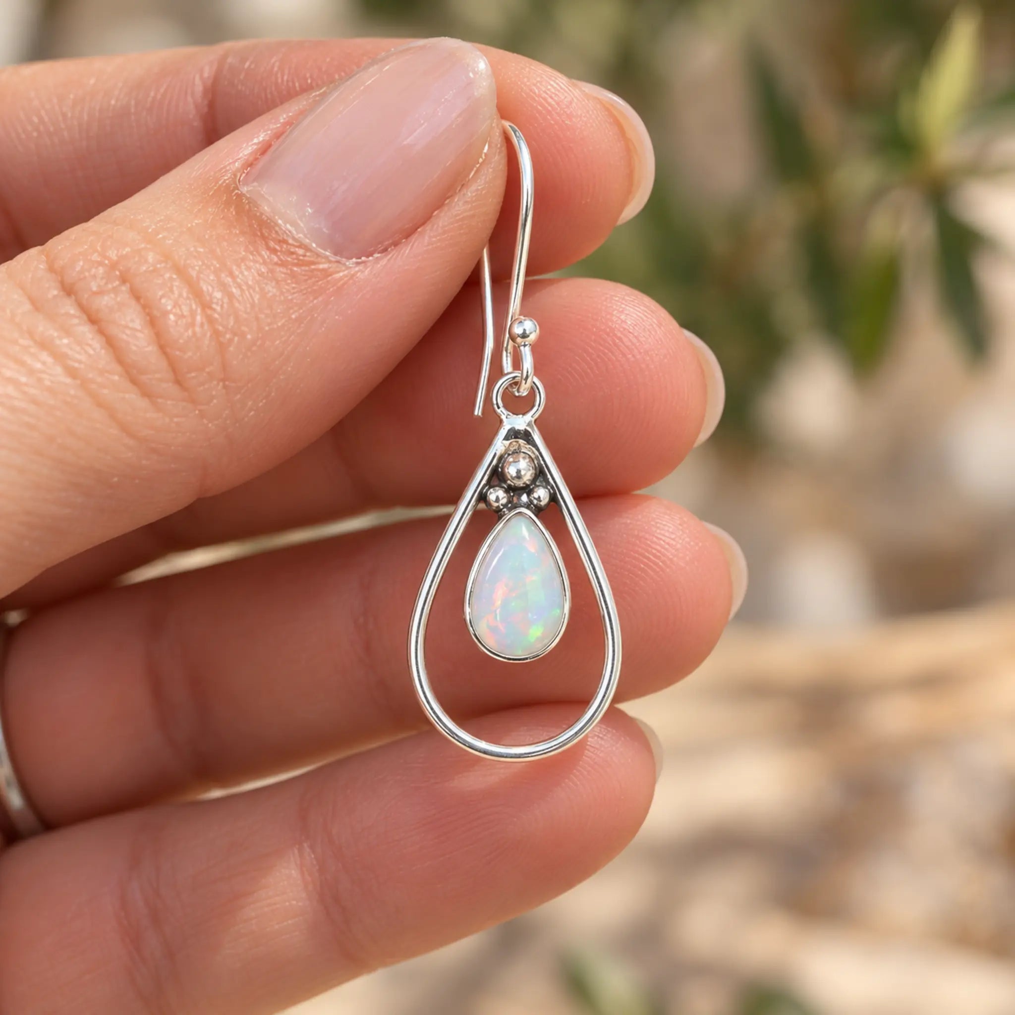 Natural opal teardrop French hook earring held between fingertips to show its size, outdoors