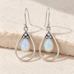 White opal teardrop French hook earrings in sterling silver with open teardrop frames, on a cream stone block