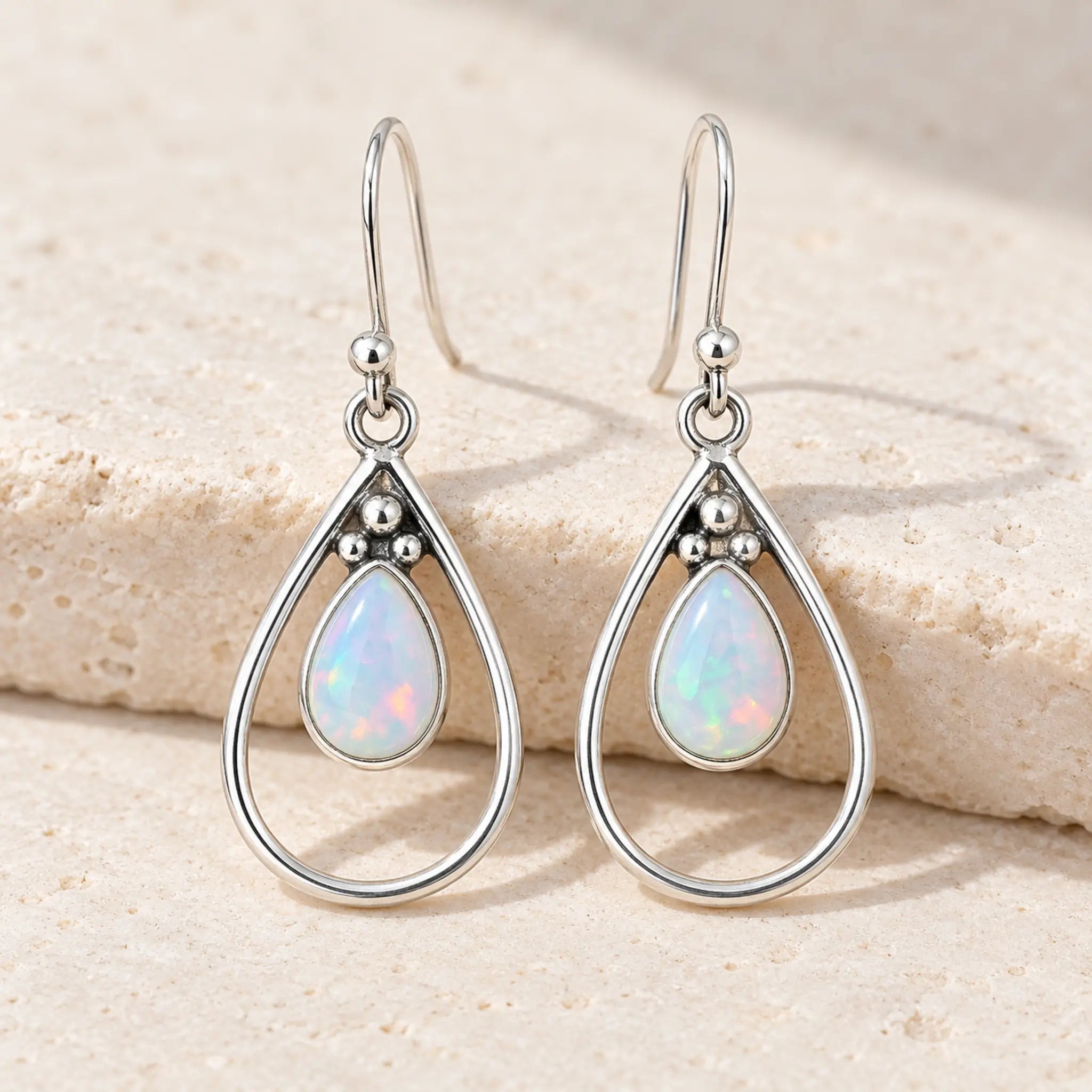 White opal teardrop French hook earrings in sterling silver with open teardrop frames, on a cream stone block