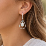 Natural opal teardrop French hook earring worn on the ear, white opal in an open sterling silver teardrop