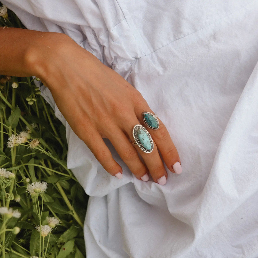 woman laying in a field of daisies wearing a white dress and two sterling silver rings with turquoise stones