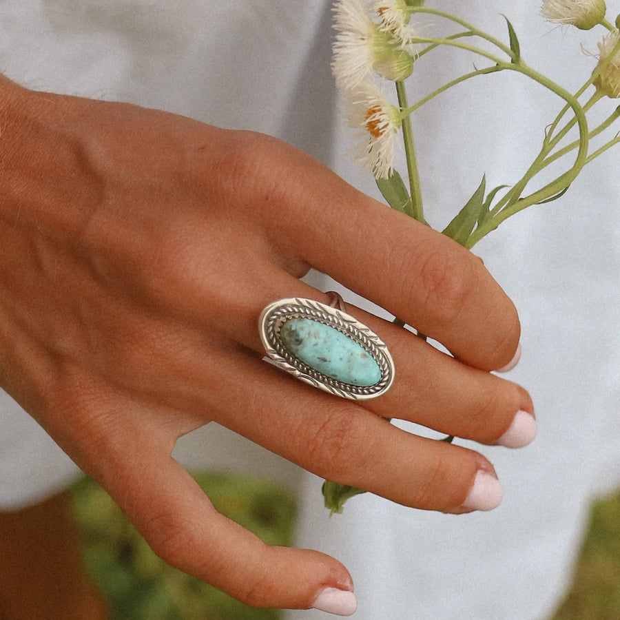 woman's hand showing her wearing a large sterling silver ring with an oval turquoise stone.