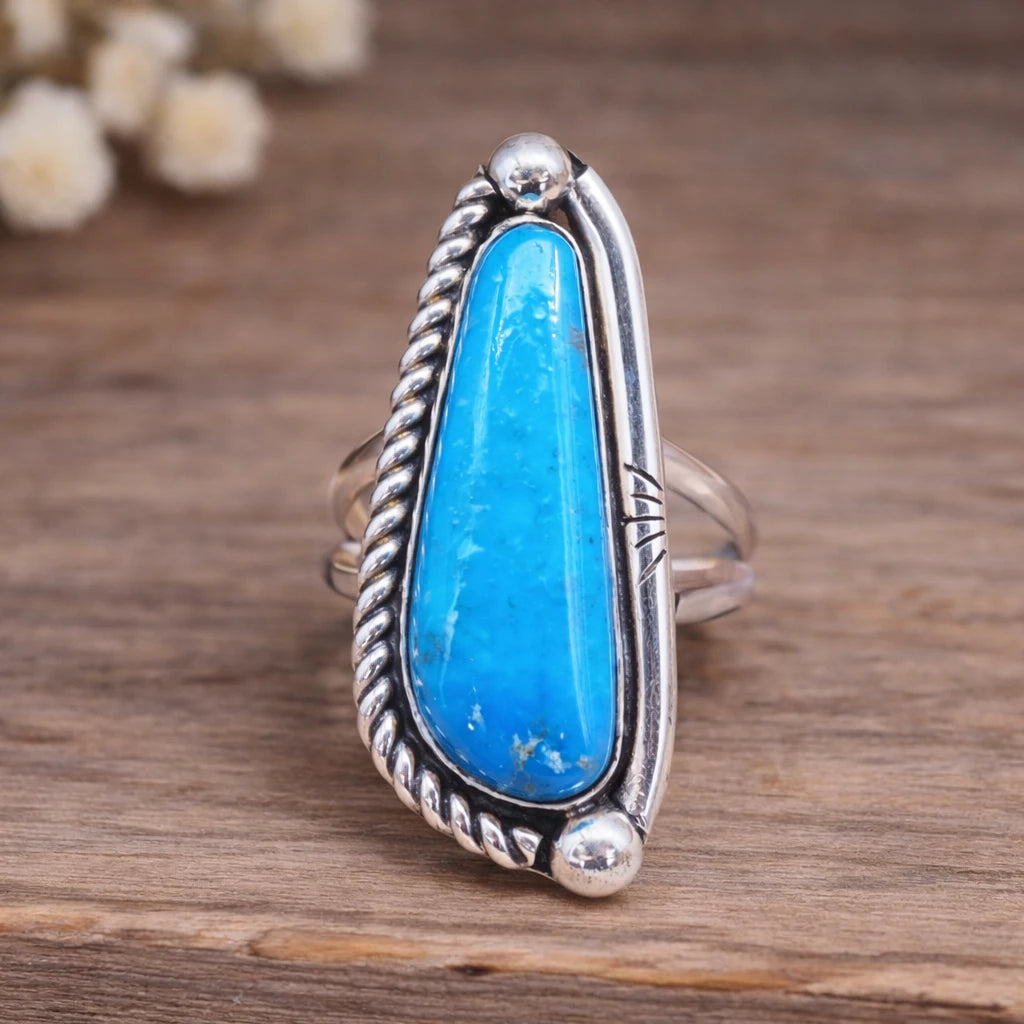 Silver ring with a large blue stone on a wooden surface