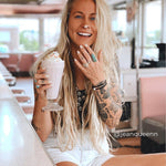 Woman with tattoos holding a milkshake in a diner wearing a turquoise ring