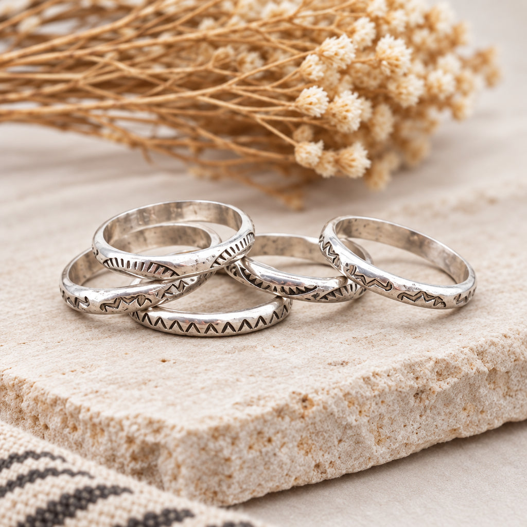 Sterling silver Navajo stamped rings on a wooden surface with dried flowers