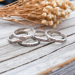 Set of silver rings on a wooden surface with dried flowers in the background
