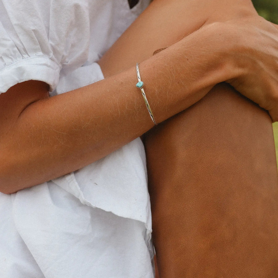 Woman sitting down wearing a white top and a silver cuff with a turquoise stone in the middle.