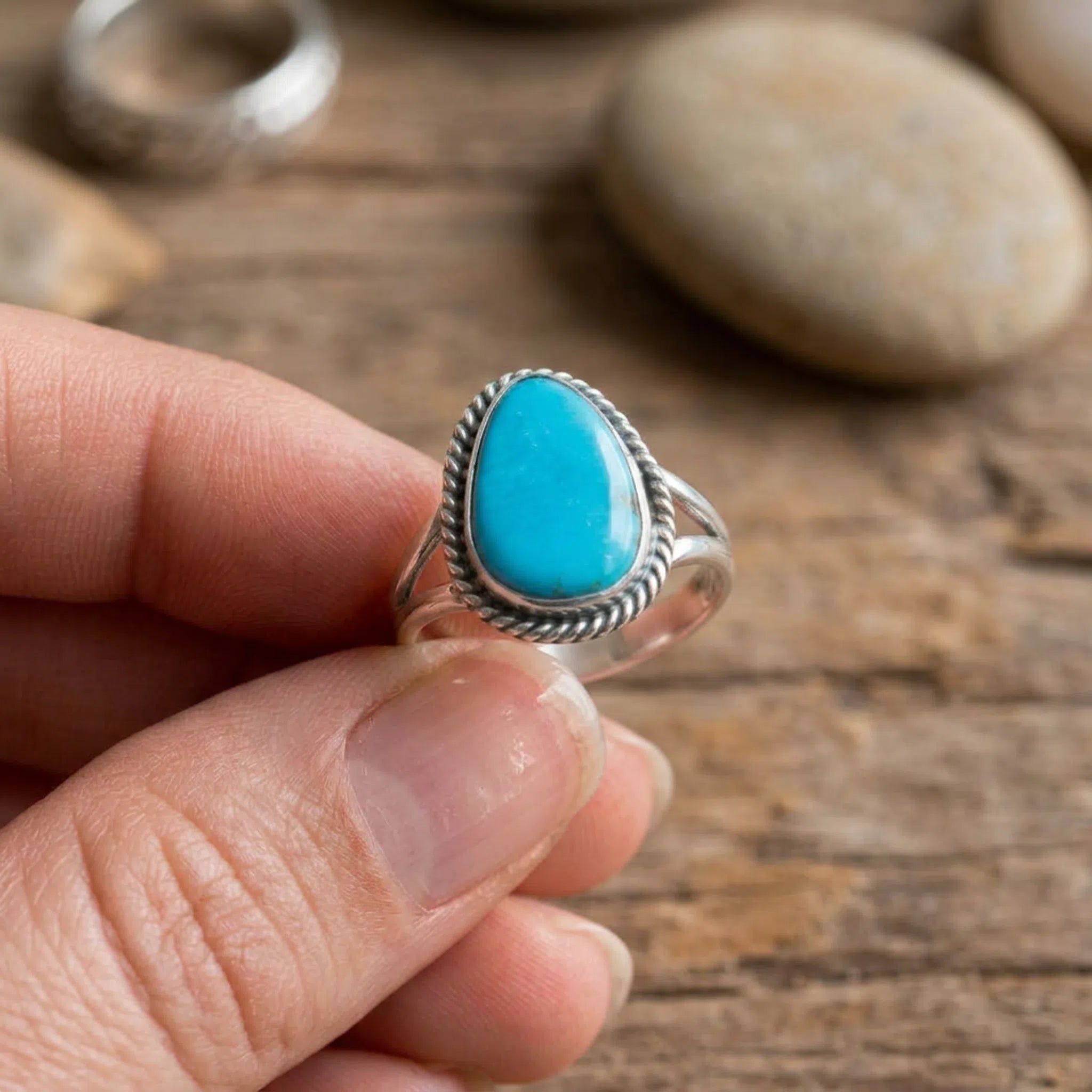 close up of fingers holding a sterling silver pear-shaped handcrafted navajo artisan ring featuring a blue natural kingman turquoise gemstone