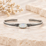 Sterling silver Navajo opal cuff bracelet with a white opal and twisted rope bands on pale stone with dried flowers