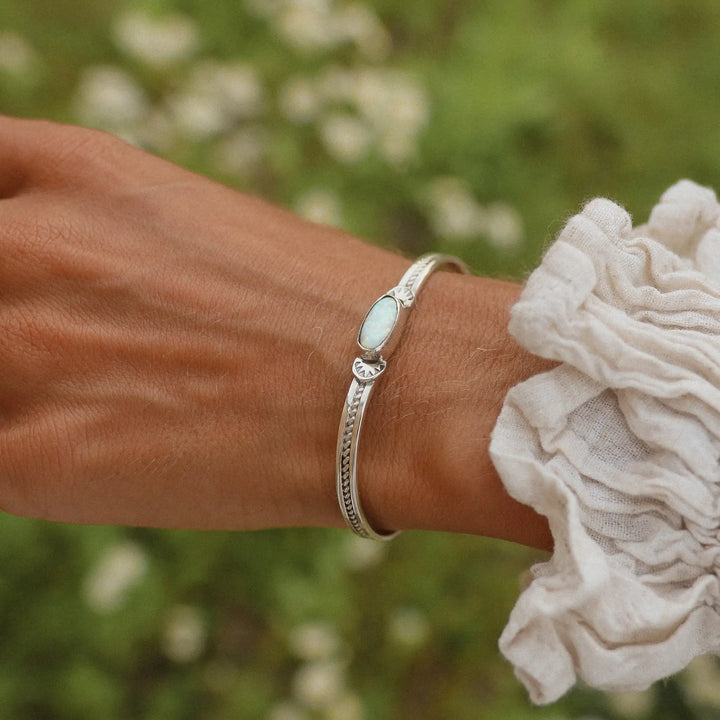 Woman wearing silver cuff bracelet with large oval opal in the centre.