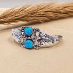 Silver bracelet with turquoise stones on a beige surface with dried grass in the background