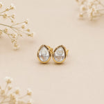 Gold teardrop earrings on a beige background with delicate flowers.