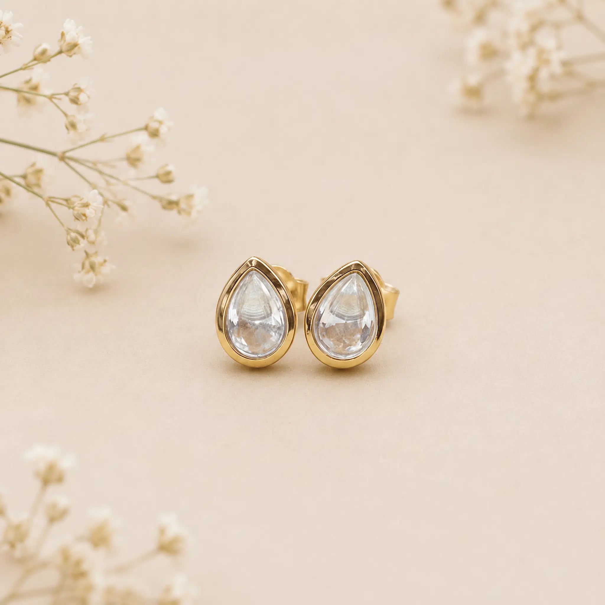 Gold teardrop earrings on a beige background with delicate flowers.