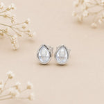 november birthstone earrings with Teardrop-shaped light blue topaz gemstones on a beige background with delicate flowers.