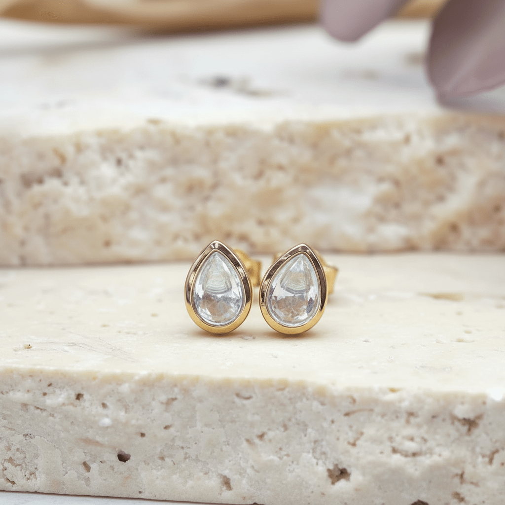 Teardrop-shaped earrings with light blue topaz gemstones on a beige surface