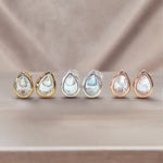 Set of six teardrop-shaped topaz earrings with silver, gold and rose gold settings on a beige background