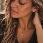 close up of a woman wearing a Gold November Birthstone Jewellery set featuring a pair of teardrop stud natural blue topaz earrings and matching natural blue topaz pendant necklace 