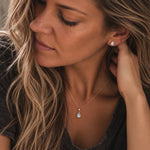 close up of a woman wearing a Rose Gold November Birthstone Jewellery set featuring a pair of teardrop stud natural blue topaz earrings and matching natural blue topaz pendant necklace 