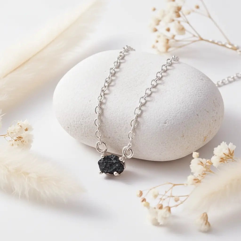 sterling Silver necklace with a raw blue diamond pendant on a white stone surface with dried flowers.