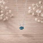 sterling Silver necklace with a raw blue diamond pendant on a wooden surface with white flowers in the background